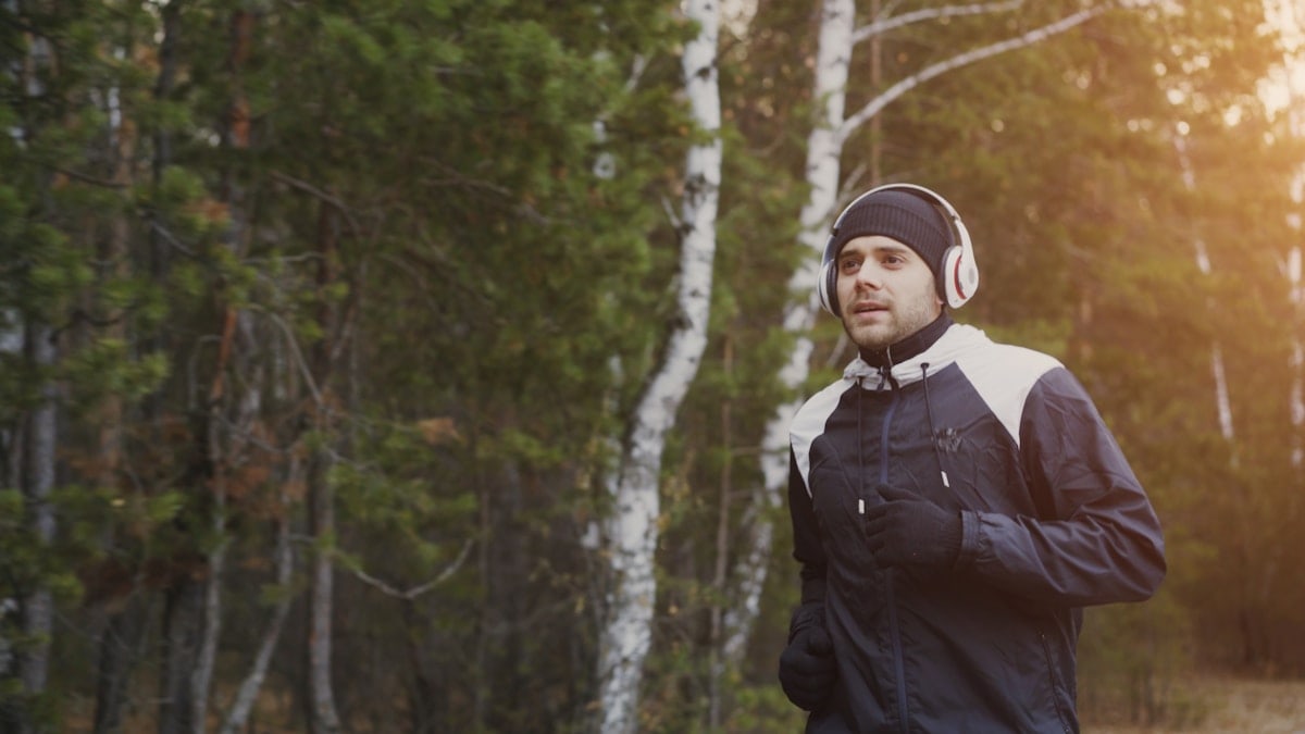 Attractive young runner man in headphones jogging while listening music in winter park in the morning